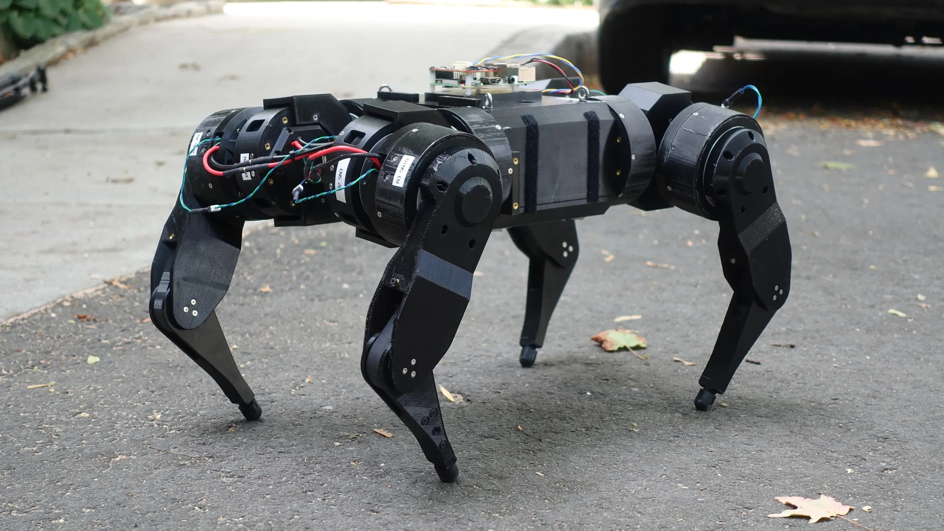 Quadruped robot platform standing on asphalt, its actuators and wiring left exposed.